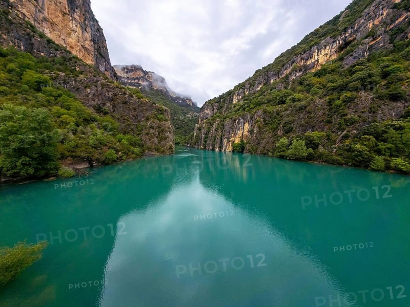 Entremon gorge on the cinca river features turquoise water flowing through a deep canyon, with steep rock cliffs and lush green vegetation under a cloudy sky in the spanish pyrenees