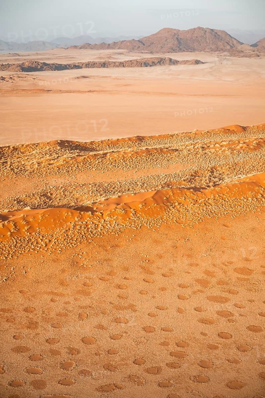 Aerial view, sand dunes with vegetation in the Namib Desert behind mountains, Namib Naukluft Park, Namibia