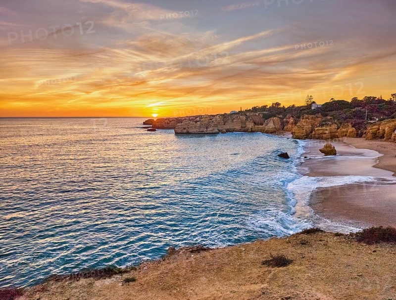 Sunset view of Praia de Sao Rafael beach with Atlantic waves, sandy cove, golden cliffs, and warm sky