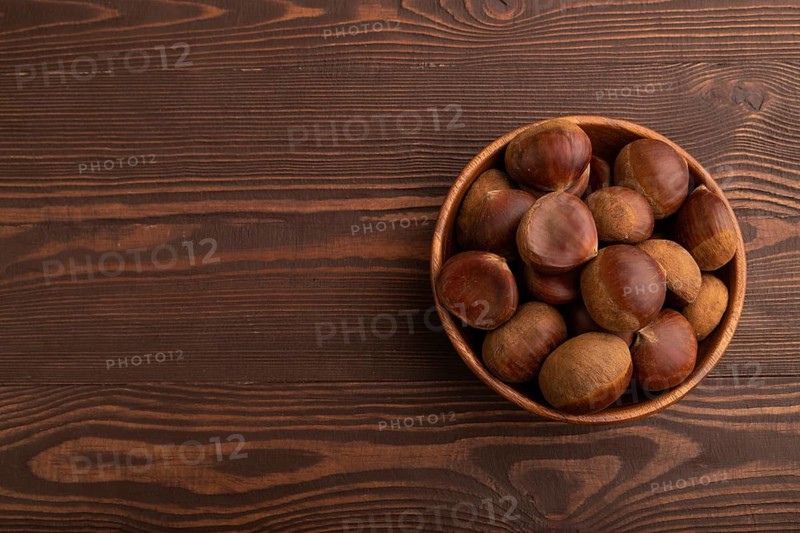 Wooden bowl with raw edible ?hestnuts on brown wooden background, top view, flat lay, copy space, minimalism