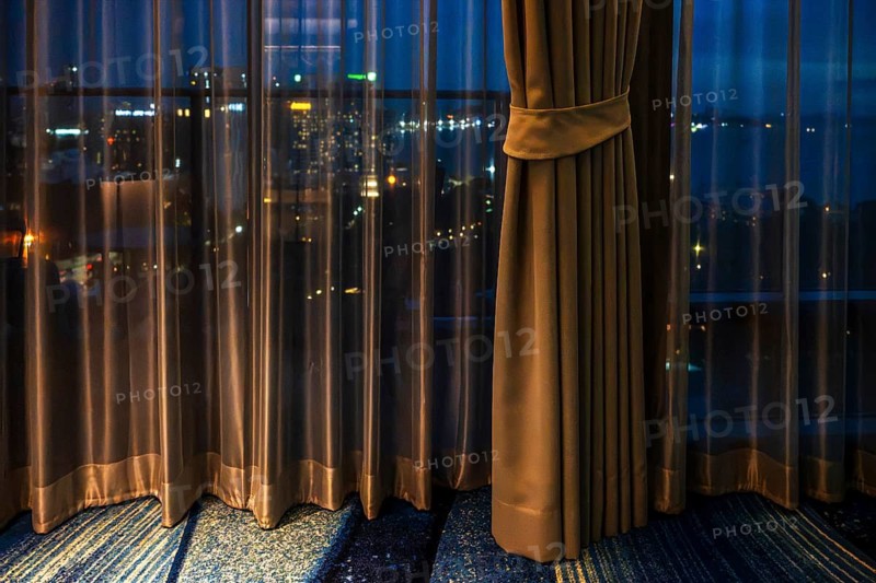 Hotel room view through curtain illuminated city scenery, Pattaya, Thailand