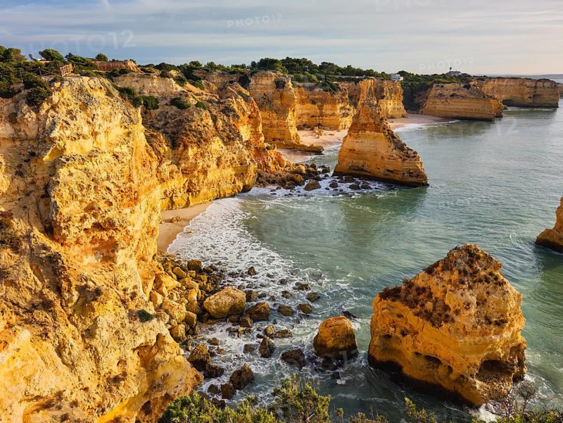 Sunrise view of Praia da Marinha beach in Algarve, Portugal, with golden cliffs, sea stacks, Atlantic waves, turquoise water, and a rocky cove