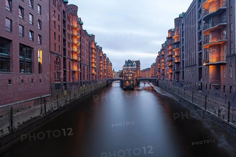 11.6.2018: Twilight view of the Wasserschloss (Water Castle) in the historic Speicherstadt district. The illuminated red brick warehouse complex and the canal are reflected in the water during the blue hour. UNESCO World Heritage site, Hamburg, Germany