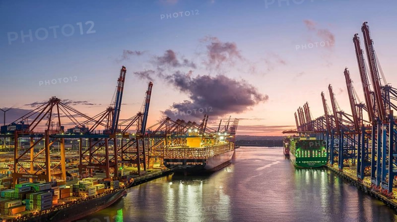 Panoramic aerial view at Waltershof harbour during the Blue Hour with Eurogate Container Terminal Hamburg (CTH) and Container Terminal Burchardkai (CTB) with the brightly lit Ever Meed, Manila Express and Fort Desaix in the background, Hamburg, Germany
