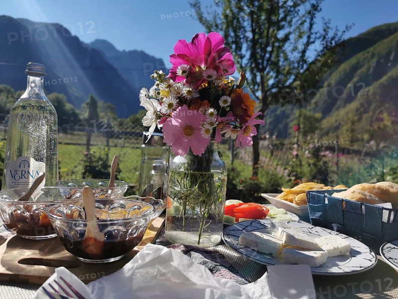 Outdoor breakfast table with flowers, cheese, marmalade and mountains in the background, Theth, Albanian Alps, Albania