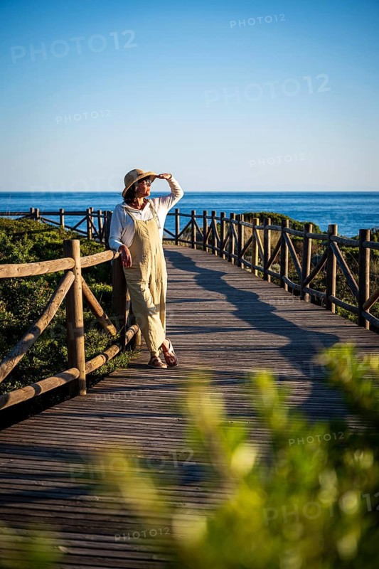 Woman, 54, wearing a sunhat looking at the sun at the Dunas de Artola, Spain