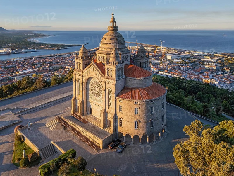 Aerial close view of Santa Luzia sanctuary in Viana do Castelo at sunrise, highlighting the ornate basilica facade, port district, and Atlantic shoreline in warm early light