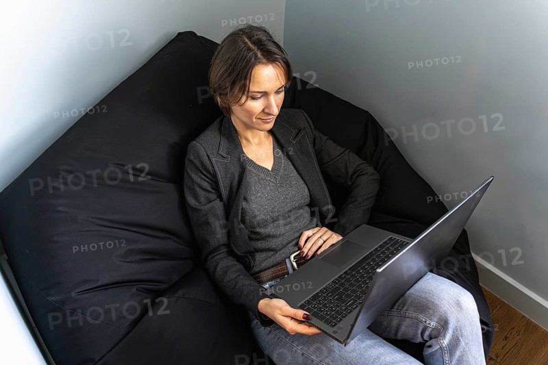 Relaxed female freelancer working on laptop from bean bag chair, top down view