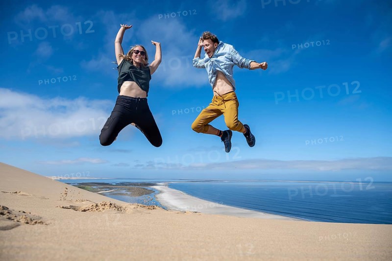 Tourists, young couple jumping in the air, stretching arms in the air, view of high dunes of the Namib Desert on the Atlantic coast, Sandwich Harbour, Namib Naukluft Park, Namib Desert, Namibia