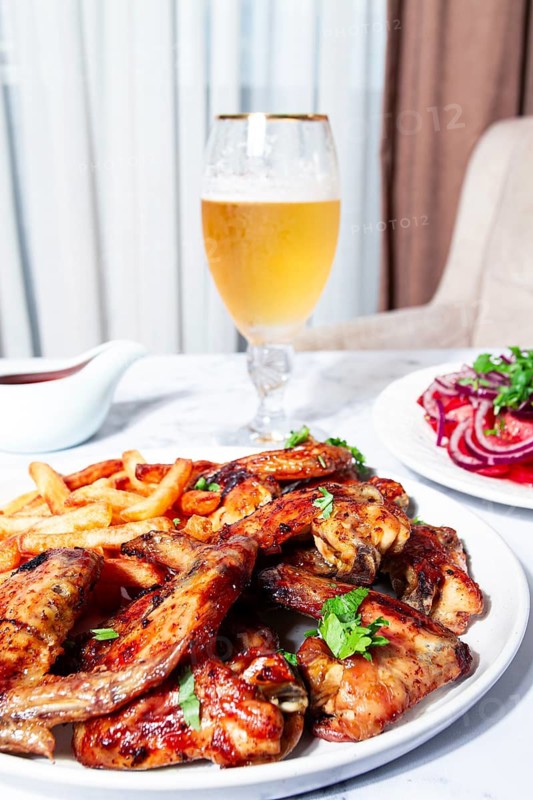 Delicious barbecue chicken wings, with French fries, salad and a refreshing drink, at a cozy table, there are no people