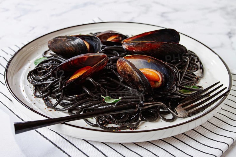 Black spaghetti with mussels, on a white plate with a fork, on a striped napkin, marble background, homemade, no people