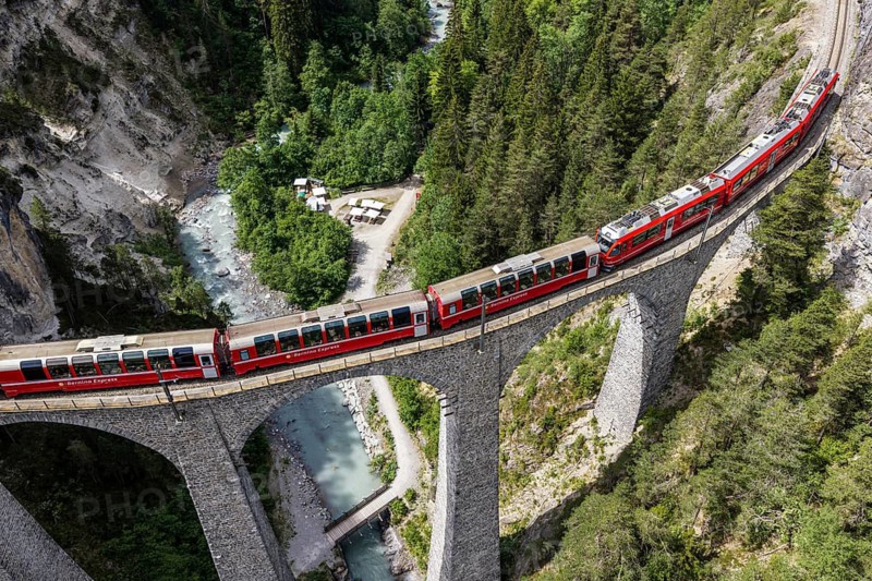 Red train of the Rhaetian railroad line, Bernina Express, passing the Landwasser Viaduct, arch bridge over Landwasser river, aerial view, Switzerland