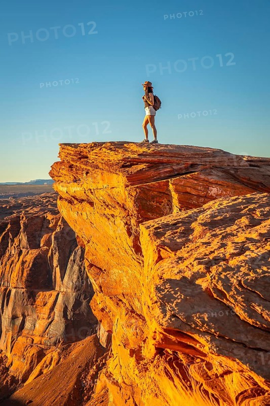 Woman stands on a canyon cliff edge at horseshoe bend, gazing over the vast arizona desert during golden hour, soaking in warm sunlight and adventurous solitude