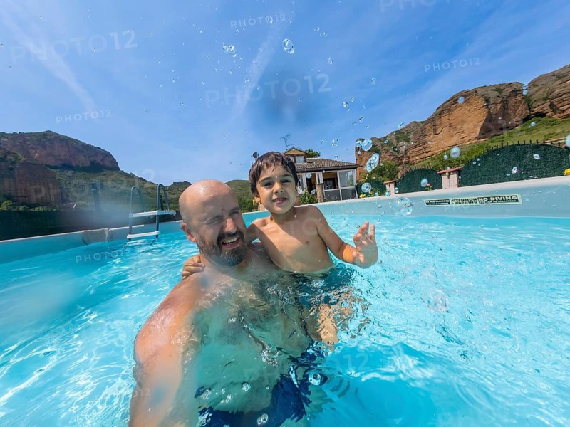 Father and son playing together in a swimming pool on a warm summer day, splashing water with joyful expressions, creating fun memories during their family vacation