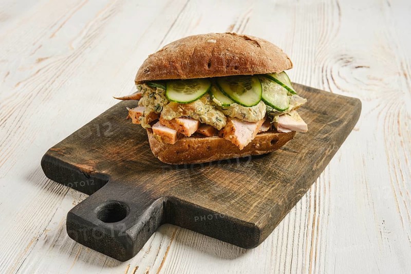 Sandwich with roasted chicken, cucumber slices and and creamy mushroom sauce with herb on wooden cutting board