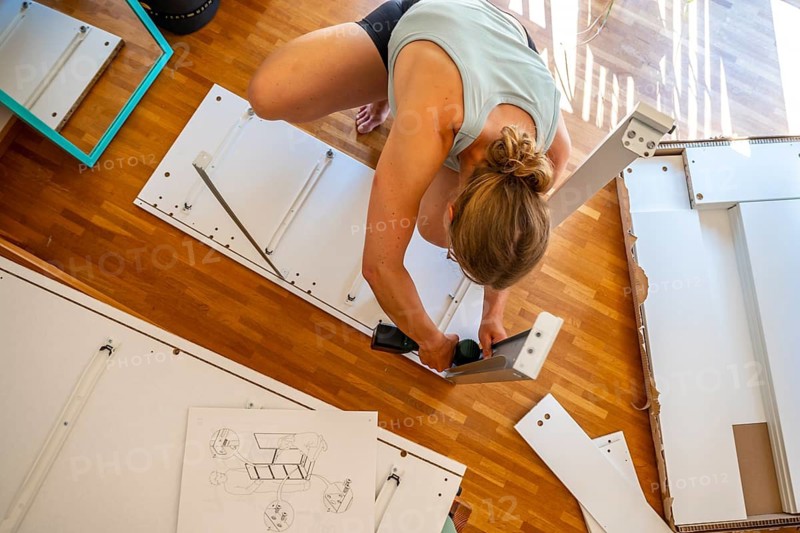 Young woman setting up a shelf, furniture assembly with screwdriver, IKEA furniture in a new apartment, moving