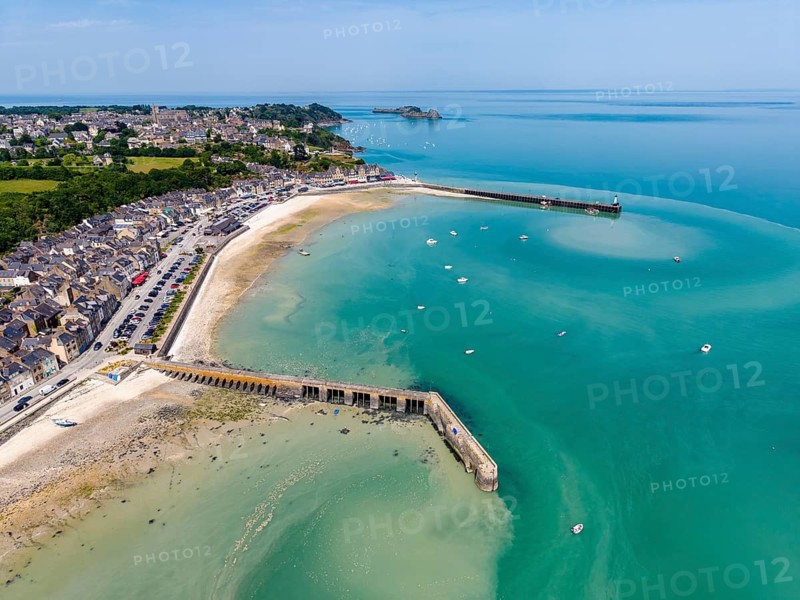 Aerial view of the picturesque fishing village of Cancale on the Emerald Coast. The picture shows the Port de la Houle harbour area at low tide with the distinctive Cale de l'Épi pier. The row of houses with numerous fish restaurants stretches along the shore. The region is world-famous for its oyster farming. In the background you can see Mont-Saint-Michel Bay, Ille-et-Vilaine department, Brittany, English Channel, France