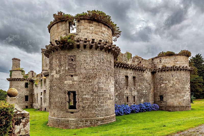 Stone castle ruins with round towers and overgrown plants under cloudy sky, The ruins of Château de Kergournadeac'h in Cléder Brittany