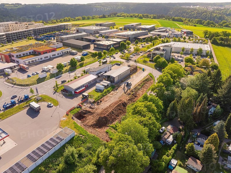 An aerial view of a construction site in an industrial area with surrounding green trees and sunny landscape, Parkhaus Bau, Calw, Germany
