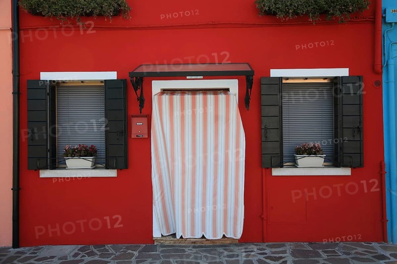 House entrance with stripe curtain and window with flowers, charming red façade, Red House on Burano Island in Venice Lagoon, Veneto, Italy