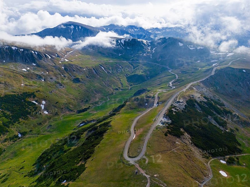 Serpentine road snakes through green mountain landscape under cloudy sky, aerial view, near Rânca, Ranca, Transalpina high road, Drum na?ional 67C, national road, Transylvania Alps, South Carpathians, Romania