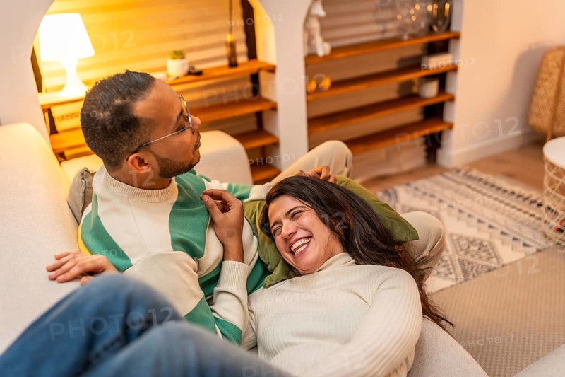 Young couple sharing a cozy moment at home, woman laughing on her partners lap in the living room, warm, relaxed intimacy and genuine connection between them