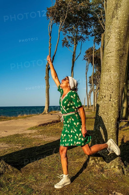 A woman (54) wearing a green tennis dress and white trainers returns an imaginary ball, Gespensterwald, Nienhagen, Germany