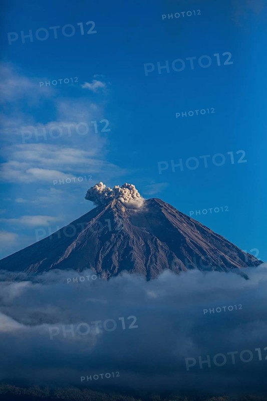 Smoke rises from the volcano as surrounding clouds and a blue sky frame the scene, Smoking Volcano, Sumatra, Jakarta, Indonesia