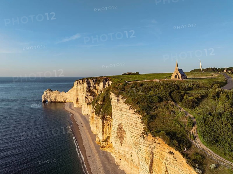 Aerial view of the Porte d'Amont rock formation and landmark, Falaise d'Amont in the evening sun with the Notre Dame de la Garde chapel, Étretat, Alabaster Coast, La Côte d'Albâtre, chalk cliffs, English Channel, Seine-Maritime, Normandy, France
