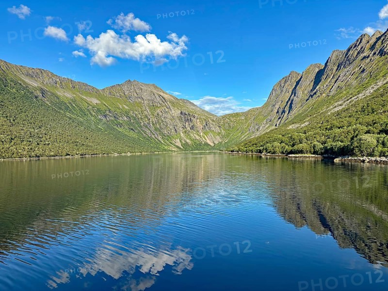 Scenic mountain landscape with calm, reflecting water and blue sky surrounded by steep mountains, Gryllefjord, Senja, Troms, Norway