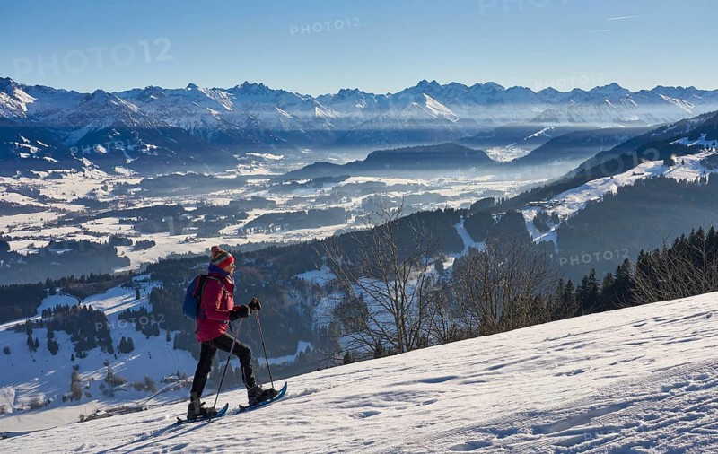 Nice and active senior woman snowshoeing in in the snow covered Allgaue alps above the valley of river Iller, Immenstadt, Bavaria, Germany