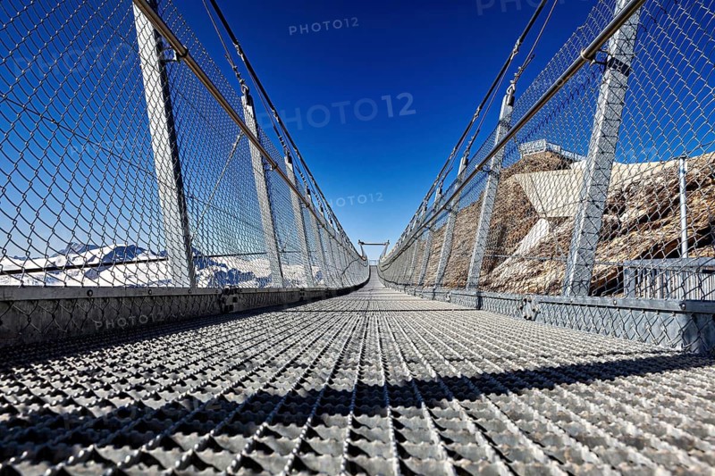 View of a metal suspension bridge against a clear blue sky in a mountainous landscape, The free-floating pedestrian suspension bridge on Mount Pilatus in Switzerland