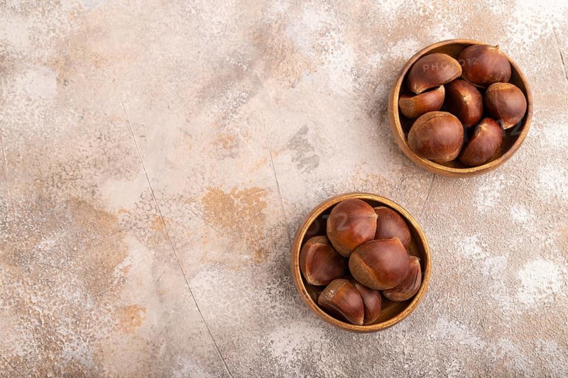 Wooden bowl with raw edible ?hestnuts on brown concrete background, top view, flat lay, copy space, minimalism