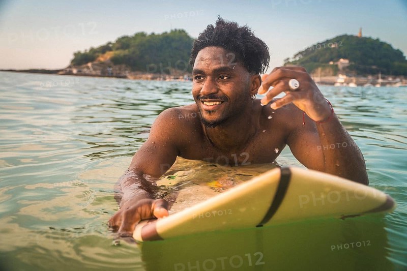 Smiling young man paddling on a surfboard in the ocean, enjoying a summer session with a retro analog style, celebrating freedom and adventure