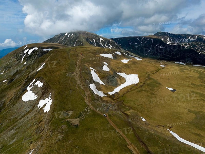 A trail runs through snow-covered mountain peaks under a cloudy sky, aerial view, Transalpina High Road, Drum na?ional 67C, National Road, Transylvania Alps, Southern Carpathians, Romania