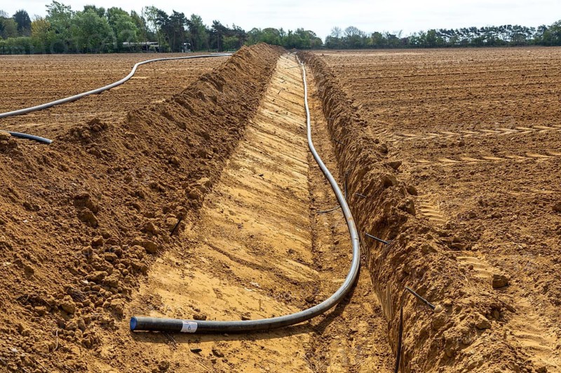Poly pipe subsurface irrigation system in excavated ditch across sandy field, Shottosham, Suffolk, England, UK
