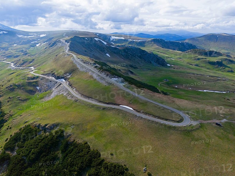 Narrow road snakes through vast green mountains under a slightly cloudy sky, aerial view, near Ranca, Transalpina High Road, Drum Na?ional 67C, National Highway, Transylvania Alps, Southern Carpathians, Romania
