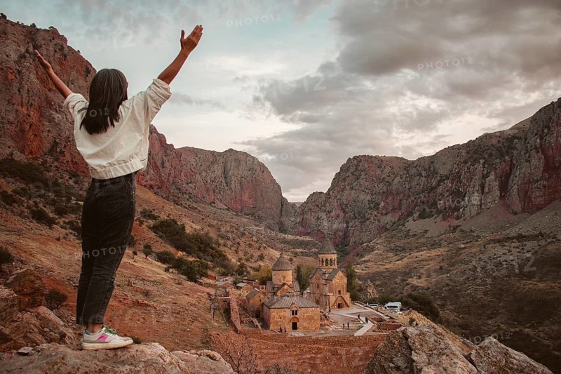 Excited happy tourist woman with outstretched arms admires the view of the famous Armenian monastery of Noravank. Travel and tourism concept