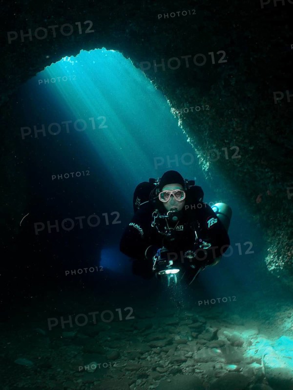 A diver with equipment explores an underwater cave illuminated by blue light rays, Fraskeric dive site, Stoja, Pula, Croatia, Mediterranean