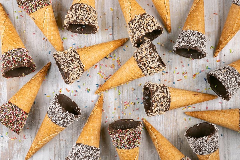 Ice cream cones with colorful sprinkles, chocolate and nuts on wooden background