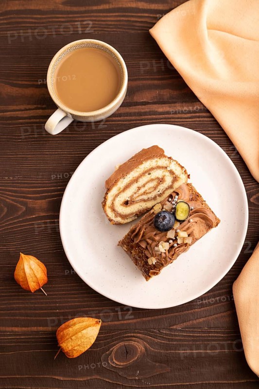 Sweet loaf with cream and caramel, cup of coffee, on brown wooden background with orange textile, close up, top view, flat lay