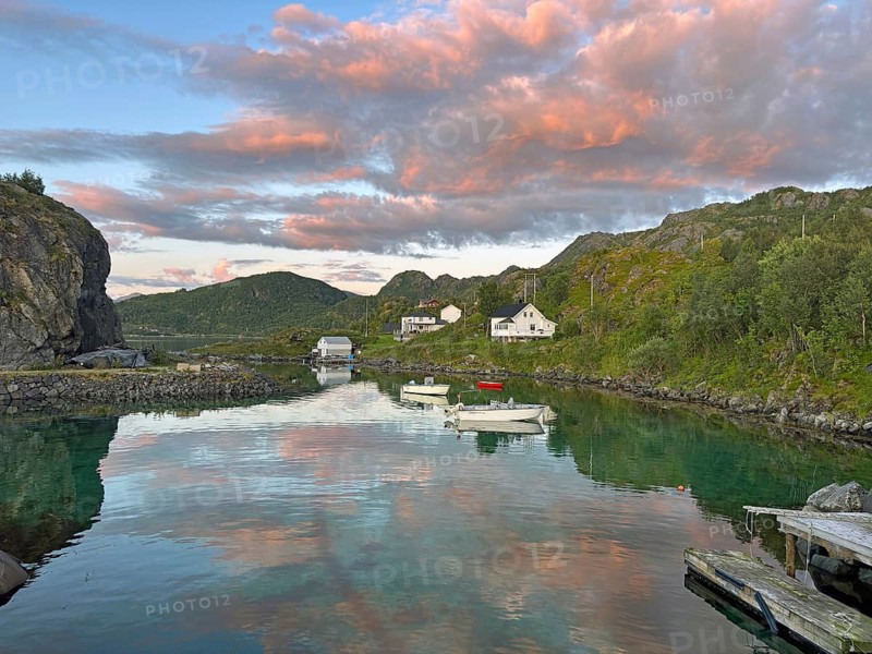 Scenic coastal village scene at sunset with boats on calm water and pink colored clouds, Hamn, Senja, Troms, Norway
