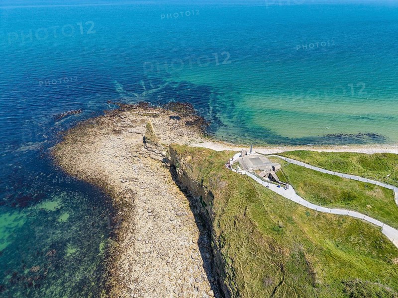 Aerial view of the historic Pointe du Hoc headland on the cliffs of Normandy. The green cliff rises prominently into the blue Atlantic. The numerous, deep bomb craters from the Second World War, which still shape the landscape today, are clearly visible. At this former base of the German Wehrmacht, a decisive battle took place on June 6, 1944 during the Allied Invasion, D-Day, Operation Overlord, Omaha Beach, Calvados Department, Normandy, English Channel, France