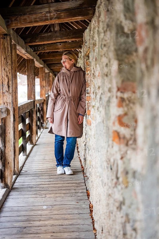 Woman leaning against a stone wall and looking around curiously in the wooden tunnel, Isny, Allgäu, Bavaria, Germany