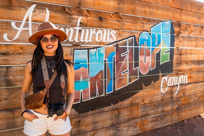 Young female traveler posing cheerfully in front of a handmade wooden sign depicting antelope canyon, embodying the spirit of travel and adventure in the american southwest