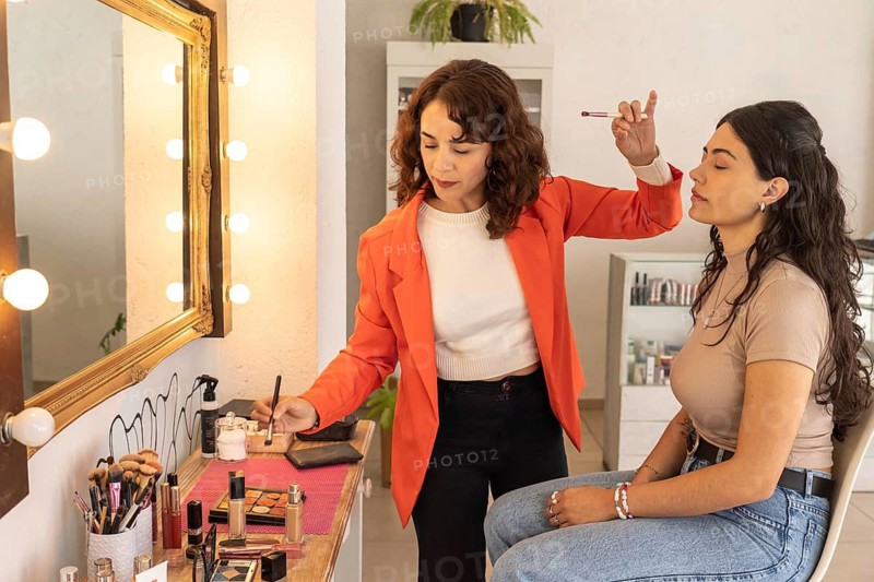 Professional makeup artist reaching for a brush while continuing makeup application on a client at a salon vanity station