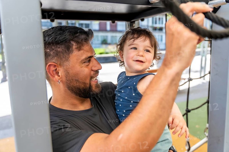 Father and son smiling and playing on a playground structure, sharing a joyful outdoor moment of bonding, affection and carefree family fun in the park