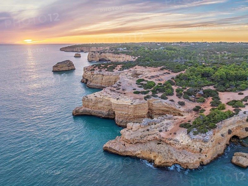 Drone sunset view of Arco de Albandeira at Praia de Albandeira in Algarve, Portugal, with limestone cliffs, Atlantic water, sea arch, and the rugged coastline stretching behind the arch