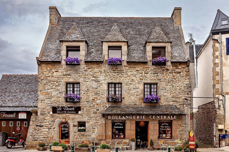 Stone commercial building with flower boxes and signs, traditional atmosphere, historic stone house in Roscoff in Brittany