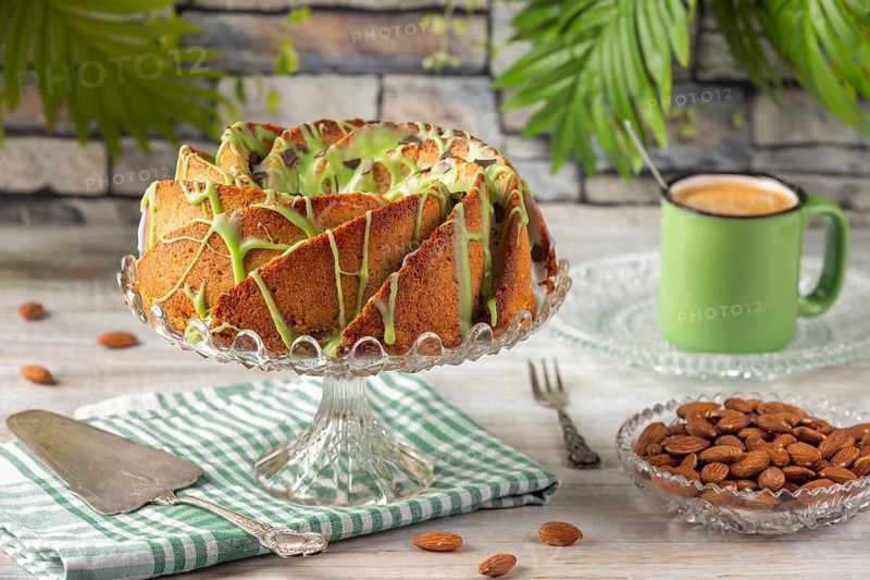 A cake with green icing next to a cup of coffee and almonds